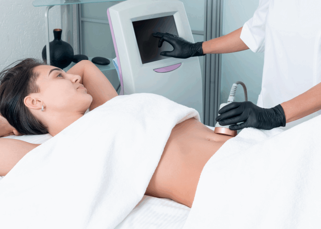 A woman undergoing laser treatment on her abdomen, with a technician assisting her in a medical environment.