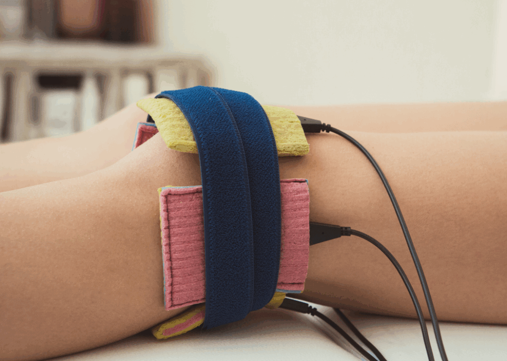 An individual applying an electric treatment device to their legs, focusing on health and wellness.